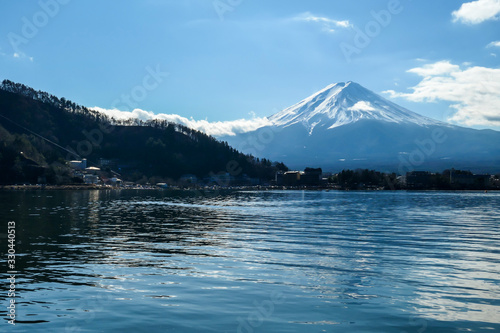 An idyllic view on Mt Fuji from the side of Kawaguchiko Lake, Japan. The mountain is surrounded by clouds. Serenity and calmness. The top of the volcano is covered with snow. Calm surface of the lake.