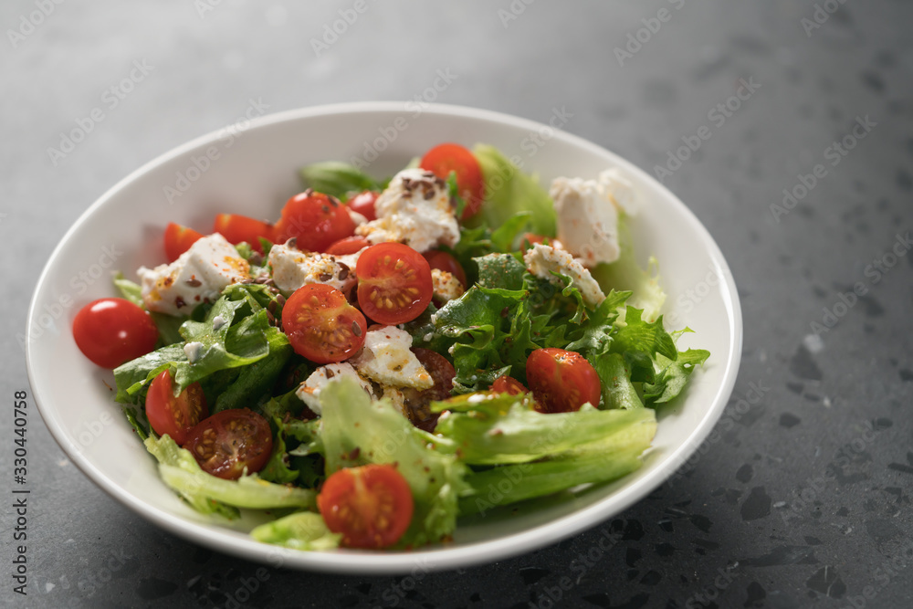Healthy light salad with cherry tomatoes, mozzarella and frisee in white bowl on concrete surface Healthy light salad with cherry tomatoes, mozzarella and frisee in white bowl on concrete surface