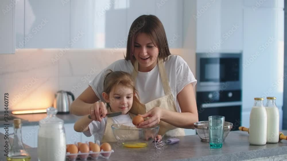 Woman and girl whisking eggs on kitchen. Daughter and mother cooking together Woman and girl whisking eggs on kitchen. Daughter and mother cooking together