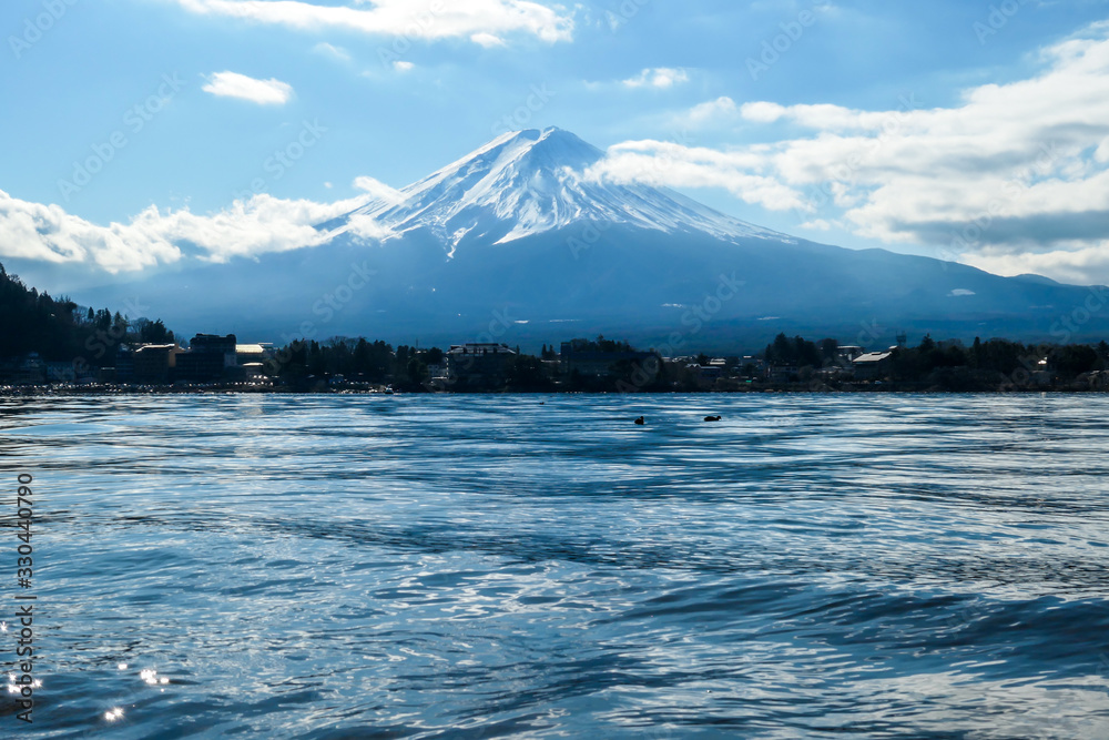 An idyllic view on Mt Fuji from the side of Kawaguchiko Lake, Japan. The mountain is surrounded by clouds. Serenity and calmness. The top of the volcano is covered with snow. Calm surface of the lake.