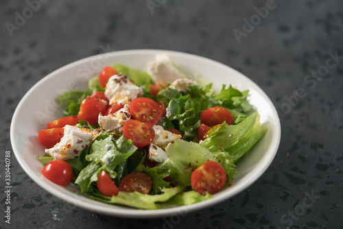 Healthy light salad with cherry tomatoes, mozzarella and frisee in white bowl on concrete surface
