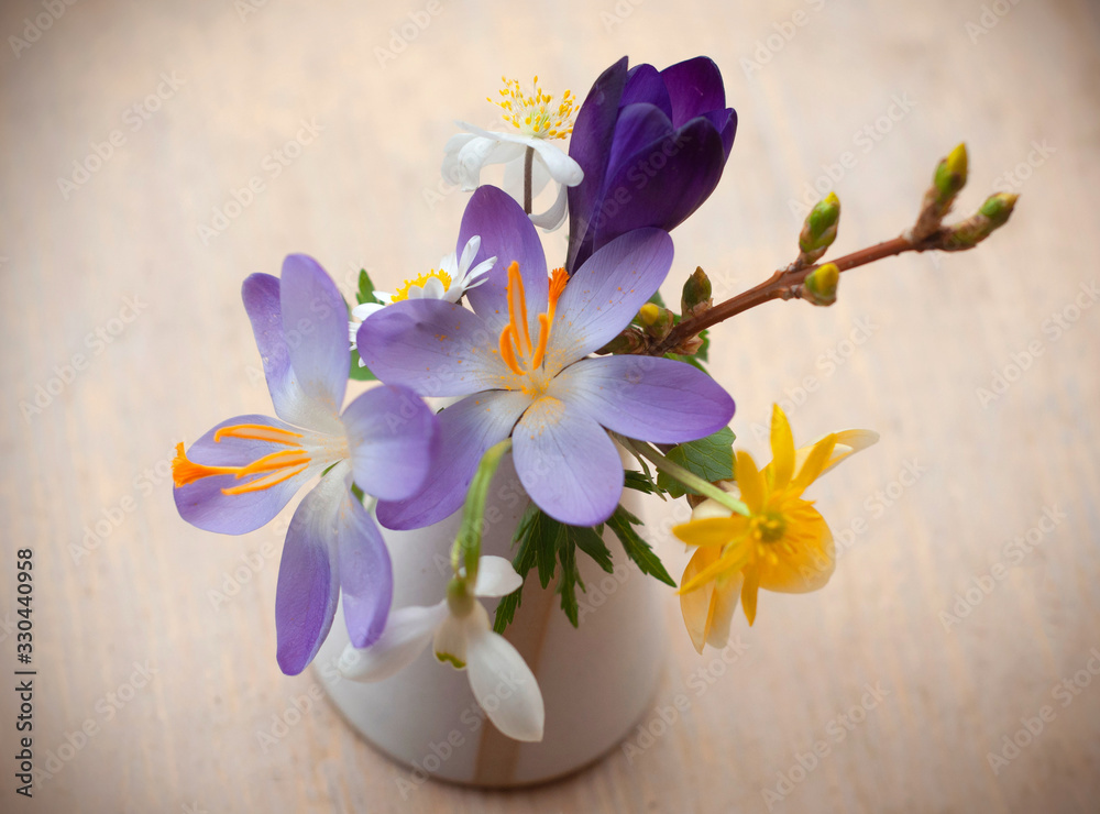 Mix of spring flowers: crocus, snowdrop and other field early flowers in a mini vase isolated on wooden background Mix of spring flowers: crocus, snowdrop and other field early flowers in a mini vase isolated on wooden background