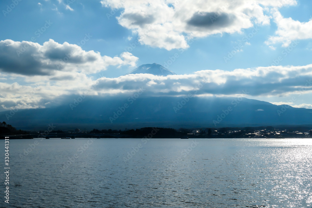 A close up view on Mt Fuji from the side of Kawaguchiko Lake, Japan. The mountain is hiding behind the clouds. Top of the volcano covered with a snow layer. Serenity and calmness. Calm lake's surface