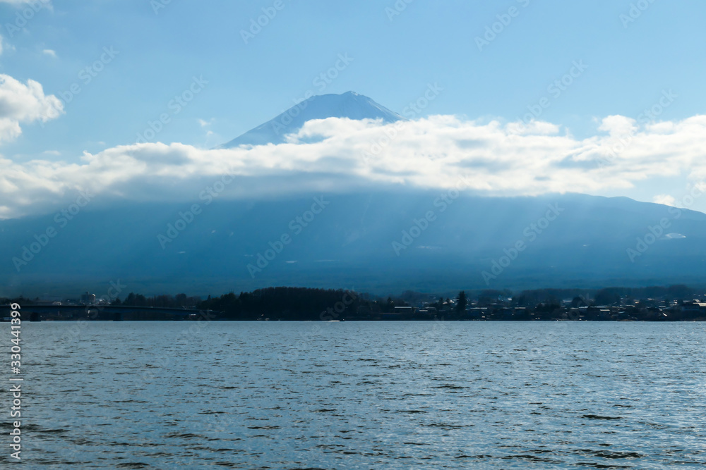 A close up view on Mt Fuji from the side of Kawaguchiko Lake, Japan. The mountain is hiding behind the clouds. Top of the volcano covered with a snow layer. Serenity and calmness. Calm lake's surface