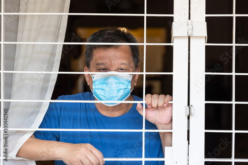 Anxious Chinese man with face mask self isolate quarantine at home for fear of contact covid-19 virus