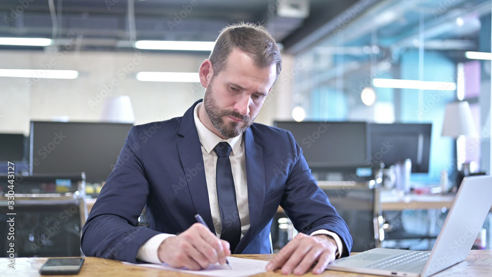 The Young Businessman writing Documents on Office Desk