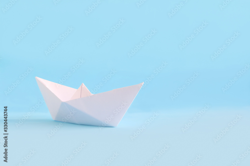 White paper handmade origami boat on the blue background. Copy space for your text. Theme of homemade toys for children. White paper handmade origami boat on the blue background. Copy space for your text. Theme of homemade toys for children.
