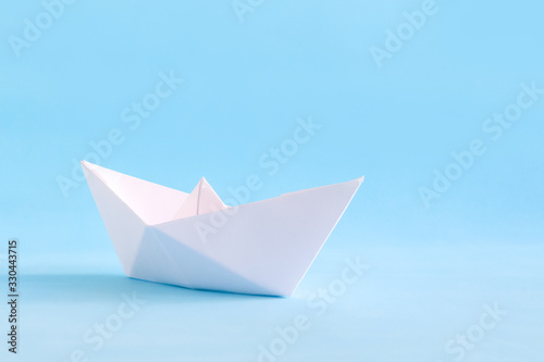 White paper handmade origami boat on the blue background. Sea summer travel theme.