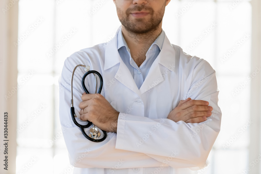 Crop close up confident male general practitioner standing with folded hands, holding stethoscope. Doctor cardiologist in white coat and professional tool ready for checkup in clinic hospital. Crop close up confident male general practitioner standing with folded hands, holding stethoscope. Doctor cardiologist in white coat and professional tool ready for checkup in clinic hospital.