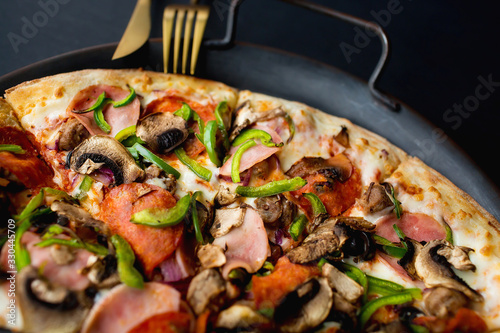 Traditional italian pizza with pepproni sausage, bacon, mushrooms, tomatoes, green pepper and cheese on a black background. View from above. Copy space for text. Restaurant menu concept.Takeaway food. photo