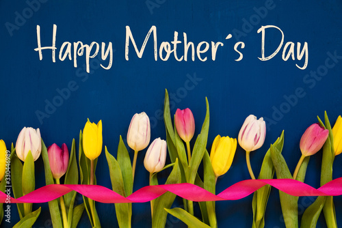 English Text Happy Mothers Day. White And Pink Tulip Spring Flowers With Ribbon. Blue Wooden Background