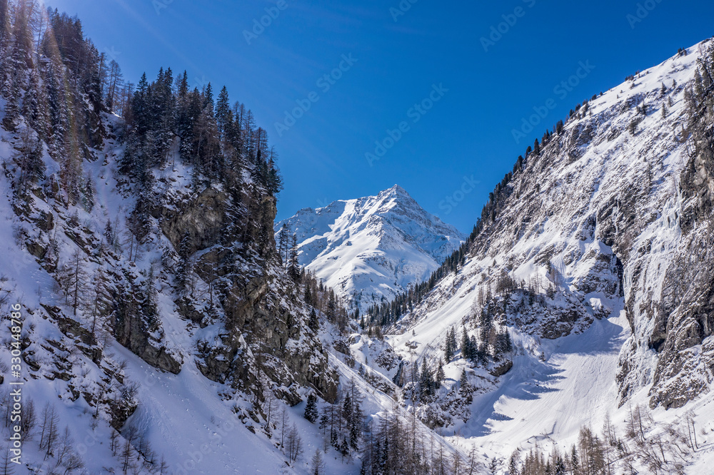Alps mountain peak beetween two mountains full of snow and spruces