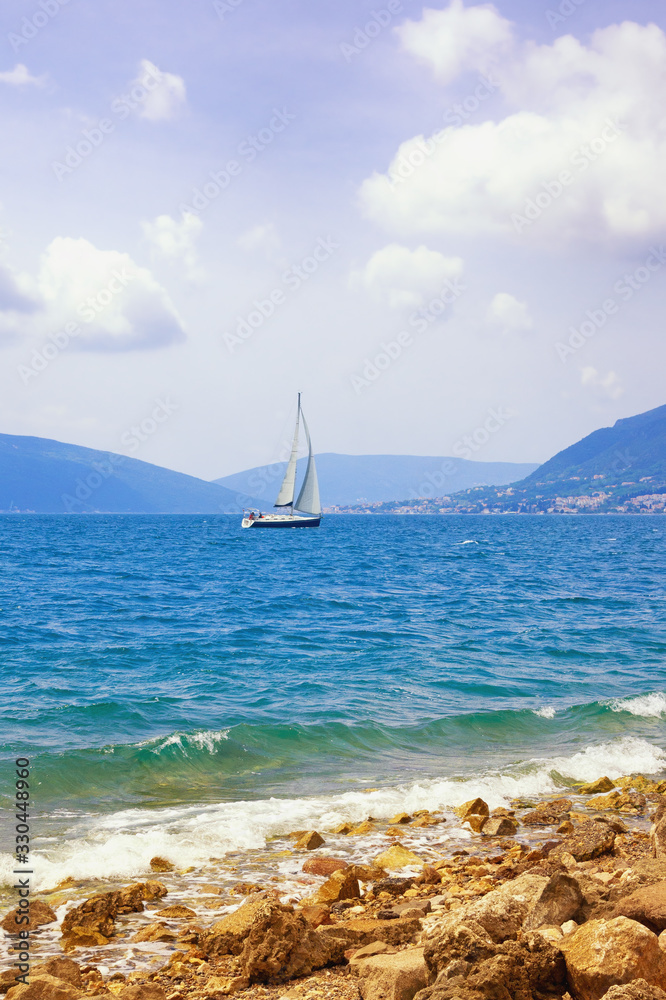 Obraz premium Beautiful Mediterranean landscape. One sailboat with white sail on water. Montenegro, Adriatic Sea. View of Kotor Bay near Tivat city. Travel concept