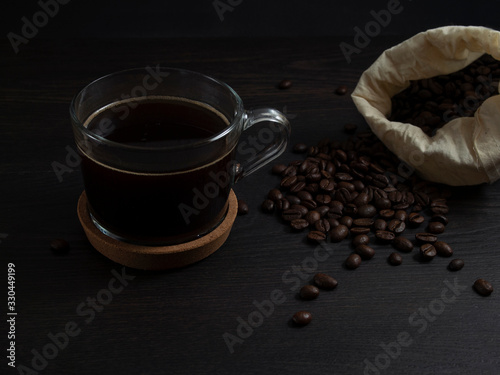 glass mug with fresh black natural coffee, a bag with coffee grains and sprinkled grains of roasted coffee on a wooden table