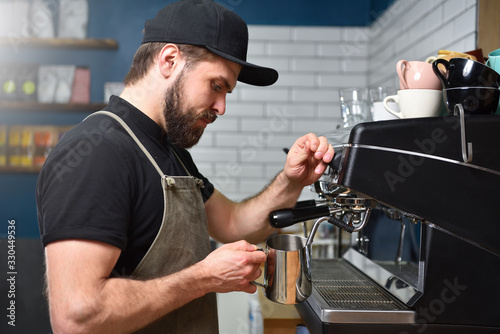 Bearded man barista making coffee on a coffee machine and whips milk with steam. Small business concept