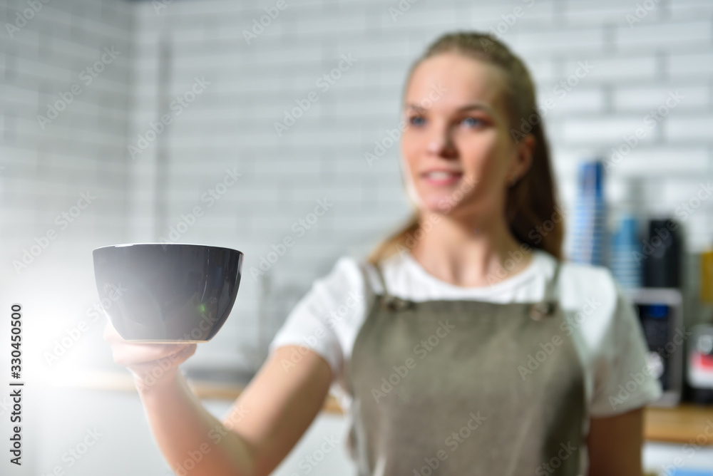 A young barista girl offers a large cup with coffee. Small business concept. A young barista girl offers a large cup with coffee. Small business concept.