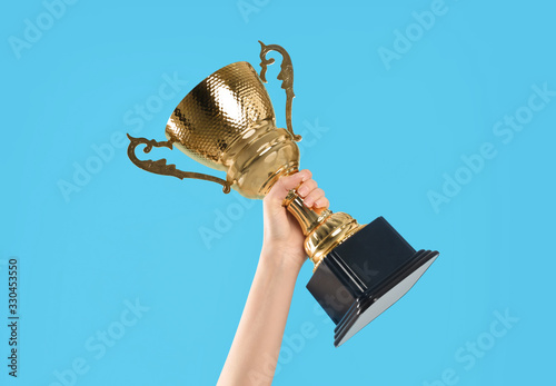 Canvas Print Woman holding gold trophy cup on light blue background, closeup