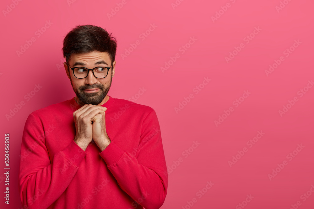 Portrait of pensive bearded man looks aside, keeps hands under chin, gazes with interest away, wears casual bright jumper and spectacles, thinks about something. Monochrome. Copy space aside for text Portrait of pensive bearded man looks aside, keeps hands under chin, gazes with interest away, wears casual bright jumper and spectacles, thinks about something. Monochrome. Copy space aside for text