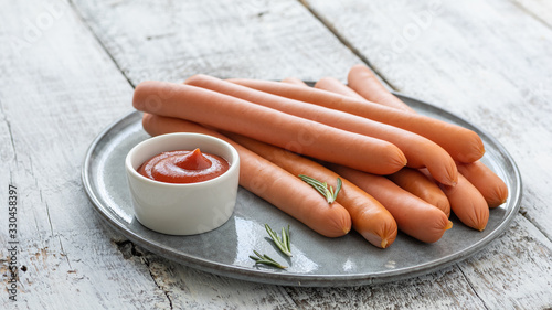 Raw frankfurter sausages with ketchup on cutting board.
