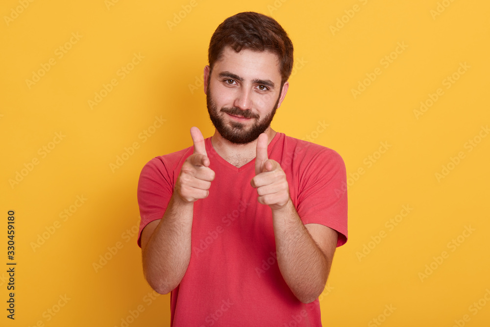Close up portrait of young attractive man wearing red t shirt, looks confident, pointing at camera with both hands, standing isolated over yellow background, handsome bearded guy wears casually. Close up portrait of young attractive man wearing red t shirt, looks confident, pointing at camera with both hands, standing isolated over yellow background, handsome bearded guy wears casually.