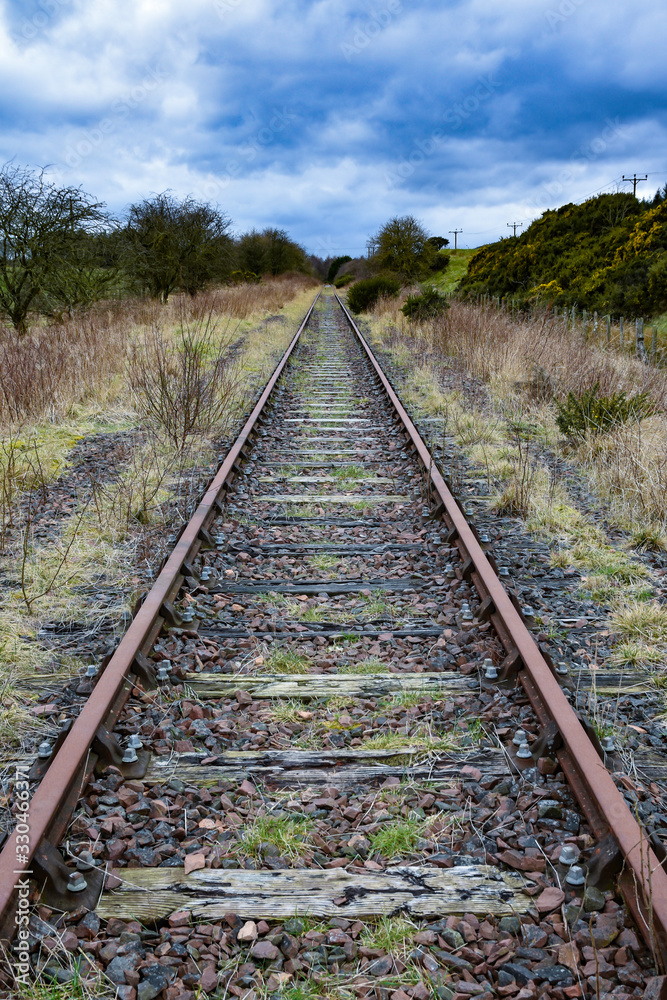 Symmetric view of abandoned railway lines leading into distance. Blue sky and clouds. Fife, Scotland, UK.