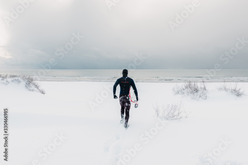 Cold winter and male surfer with surfboard. Snowy weather day with surfer in wetsuit.