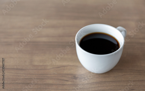 hot coffee cup on wooden table with soft-focus and over light in the background
