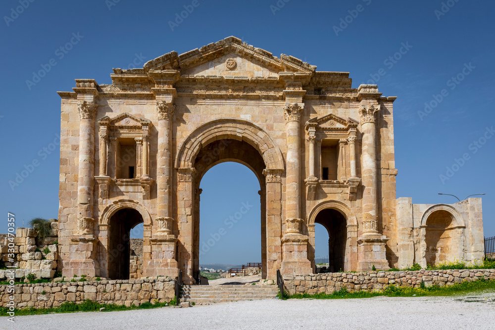 Arch of Hadrian at the roman ruins of Jerash, Jordan. Front view on a sunny day with blue sky. It features some unconventional, possibly Nabataean, architectural features, such as acanthus bases.