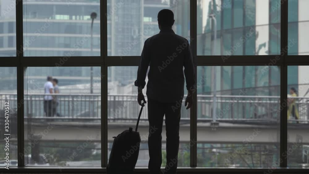 Commuter with luggage in glass building corridor to airport office Commuter with luggage in glass building corridor to airport office
