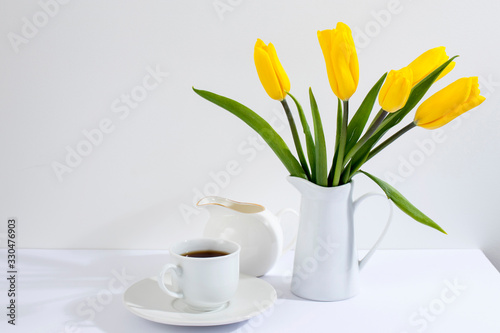 bouquet of yellow tulips is on the table opposite white wall.