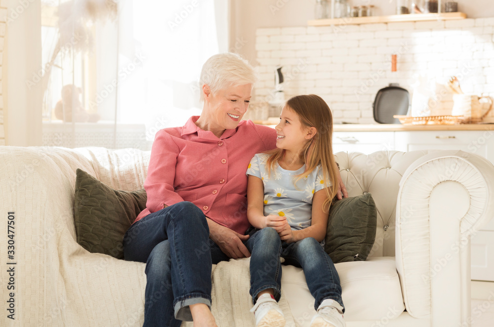 Happy granny with her granddaughter resting together on comfortable sofa indoors