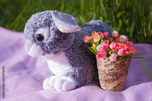 Easter decorative elements  vase with artificial flowers  plaid and bunny toy on green grass background.