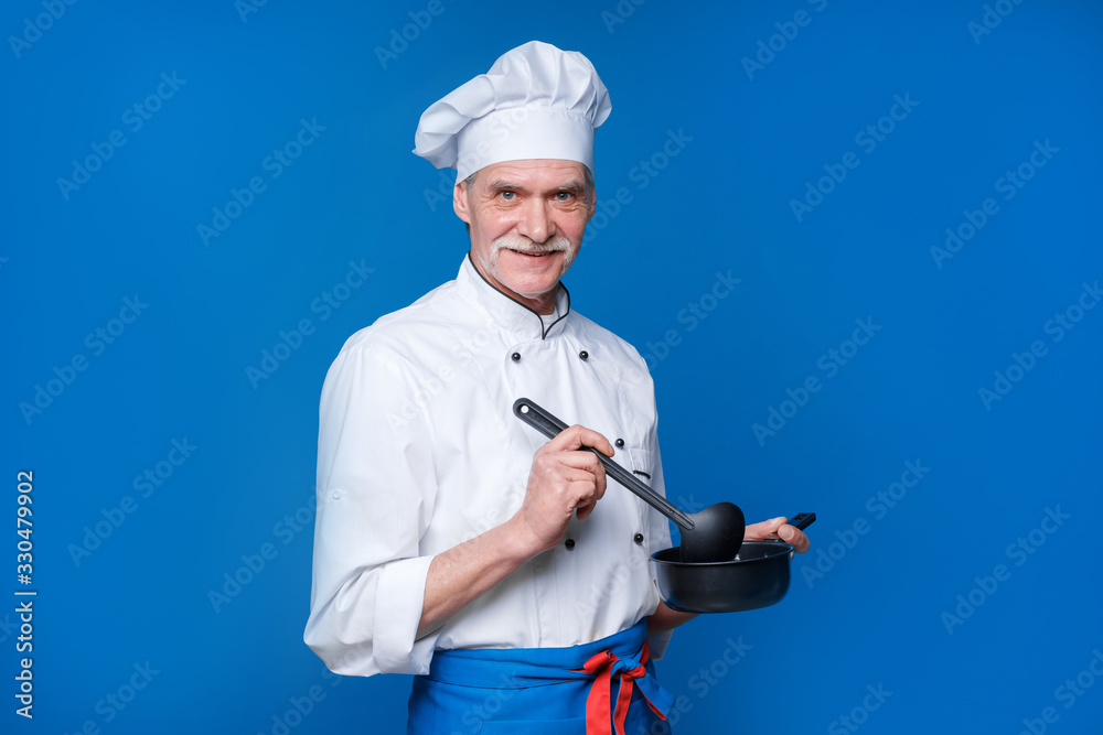 Senior man with beard cook with excited face in uniform with ladle, restaurant cuisine concept. Chef tastes soup on blue background Senior man with beard cook with excited face in uniform with ladle, restaurant cuisine concept. Chef tastes soup on blue background