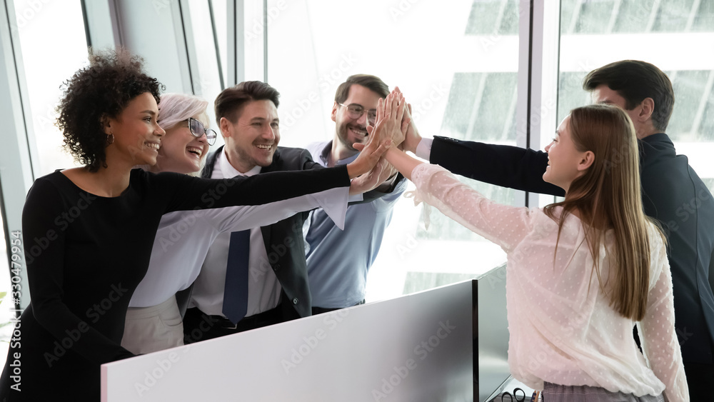 Overjoyed multiracial businesspeople give high five engaged in teambuilding activity or training at workplace, happy diverse colleagues employees show unity and support at work, partnership concept - obrazy, fototapety, plakaty 