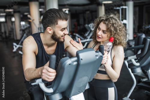 A man and a woman are speaking after training. Man resting after workout sitting on the sports equipment in the gym