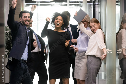 Fototapeta Naklejka Na Ścianę i Meble -  Overjoyed diverse businesspeople triumph have fun dancing in modern office corridor, happy multiracial colleagues coworkers celebrate business success together, engaged in Friday fun party at work