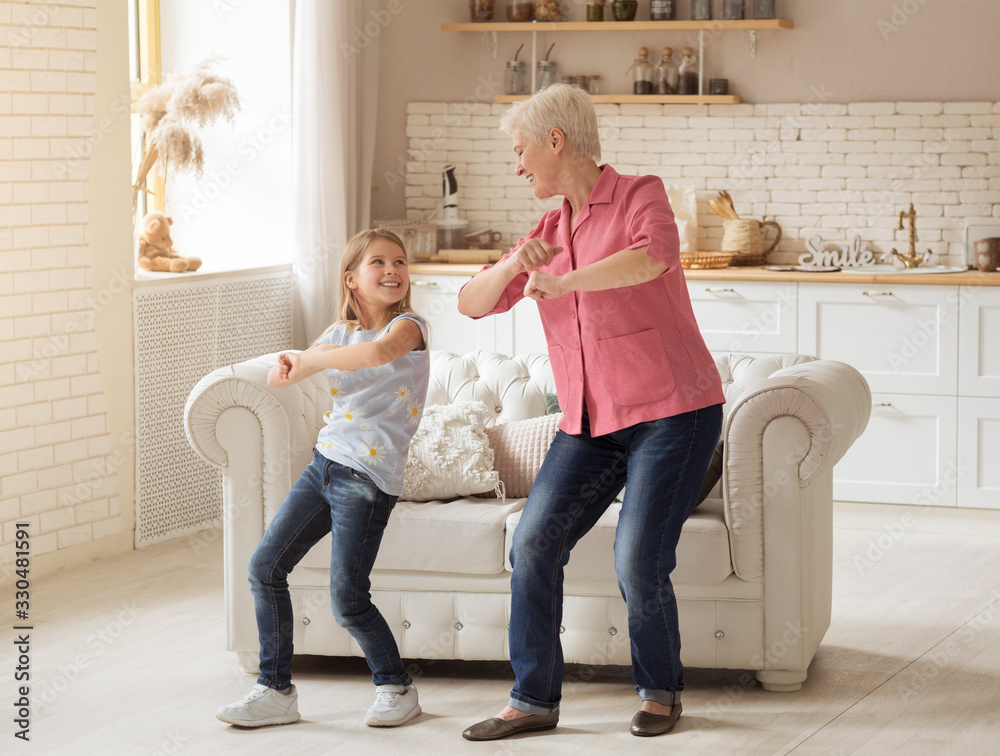Cheerful older lady with her granddaughter dancing at home - obrazy, fototapety, plakaty 