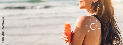 фотографія Woman wearing two piece bikini applying suncream with sun drawn on back and holding sunscreen lotion on the tropical beach