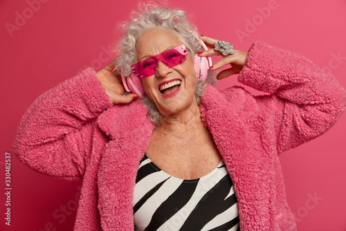 Fényképezés Horizontal shot of carefree happy senior mature lady enjoys listening favorite m