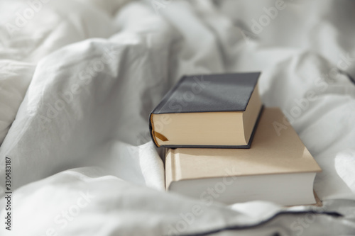 two books gray and beige on a white bedding quilt and sunbeams