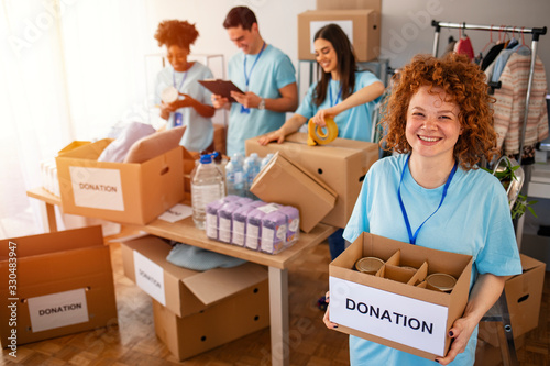 We are successful team of social workers. Woman volunteer holding a donation box and is smiling at the camera. Volunteers are helping people in the background. photo