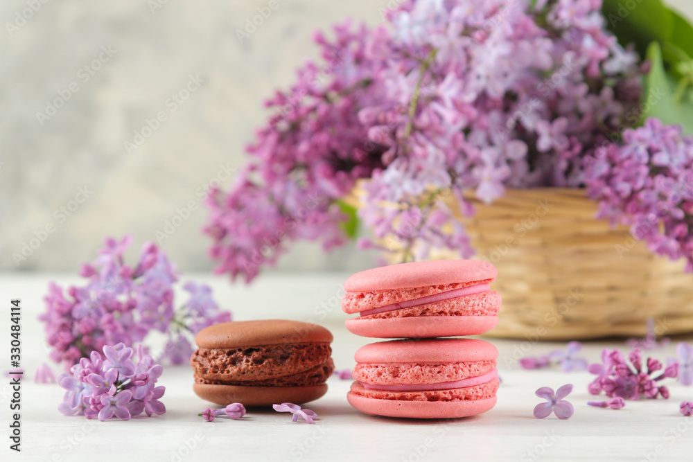 Spring flowers. Twigs of blooming lilac in a wicker basket and macaroon cake on a light concrete background Spring flowers. Twigs of blooming lilac in a wicker basket and macaroon cake on a light concrete background