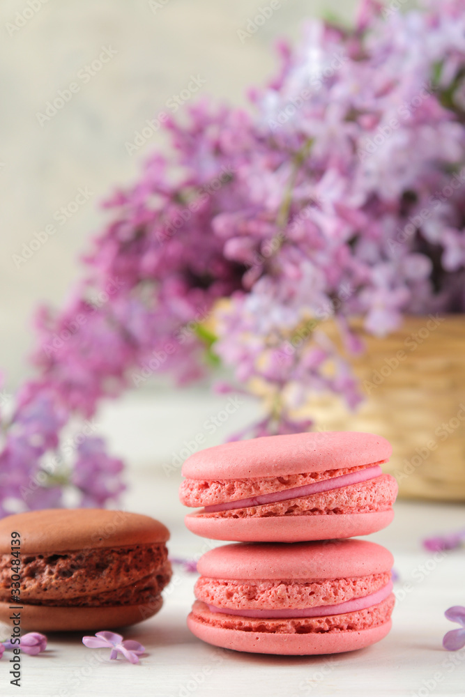 Spring flowers. Twigs of blooming lilac in a wicker basket and macaroon cake on a light concrete background Spring flowers. Twigs of blooming lilac in a wicker basket and macaroon cake on a light concrete background