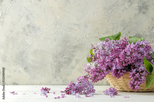 Spring flowers. Twigs of blooming lilac in a wicker basket on a light concrete background