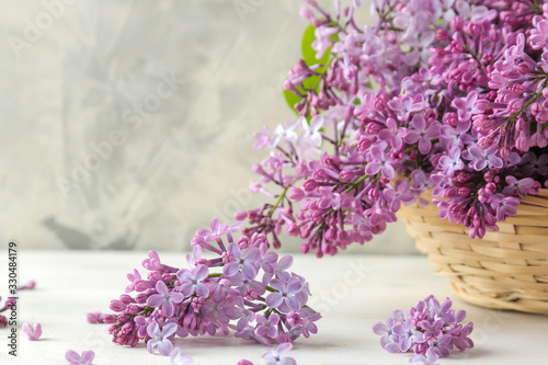 Spring flowers. Twigs of blooming lilac in a wicker basket on a light concrete background