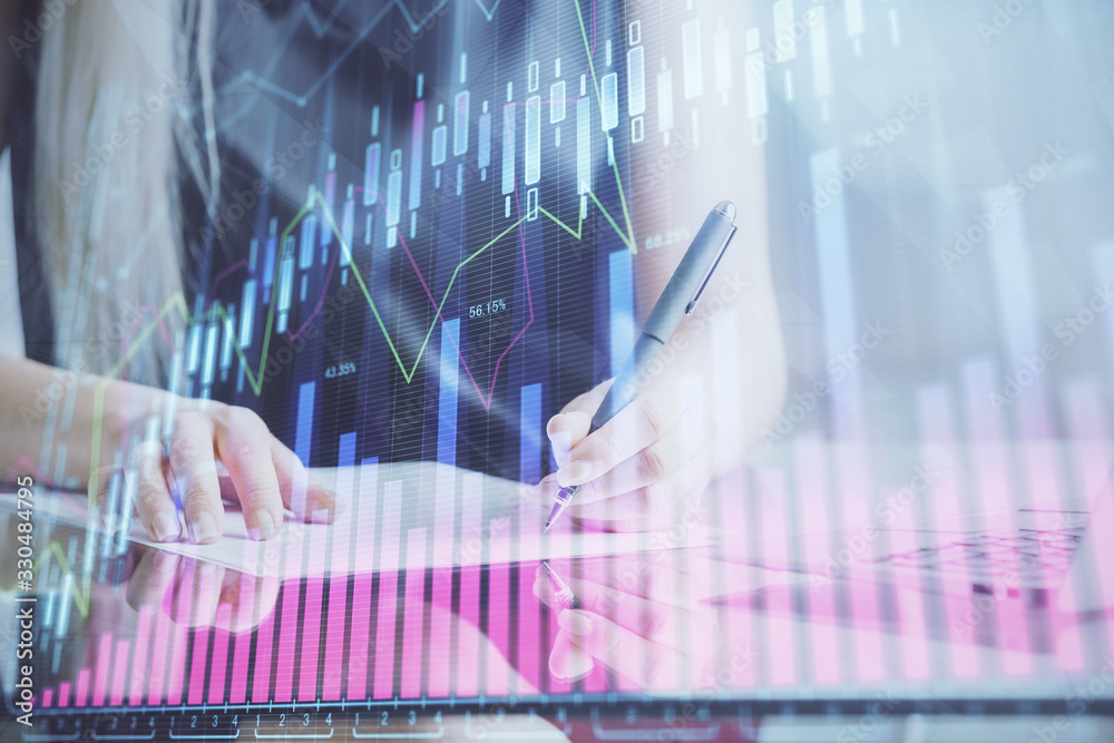 A woman hands writing information about stock market in notepad. Forex chart holograms in front. Concept of research. A woman hands writing information about stock market in notepad. Forex chart holograms in front. Concept of research.