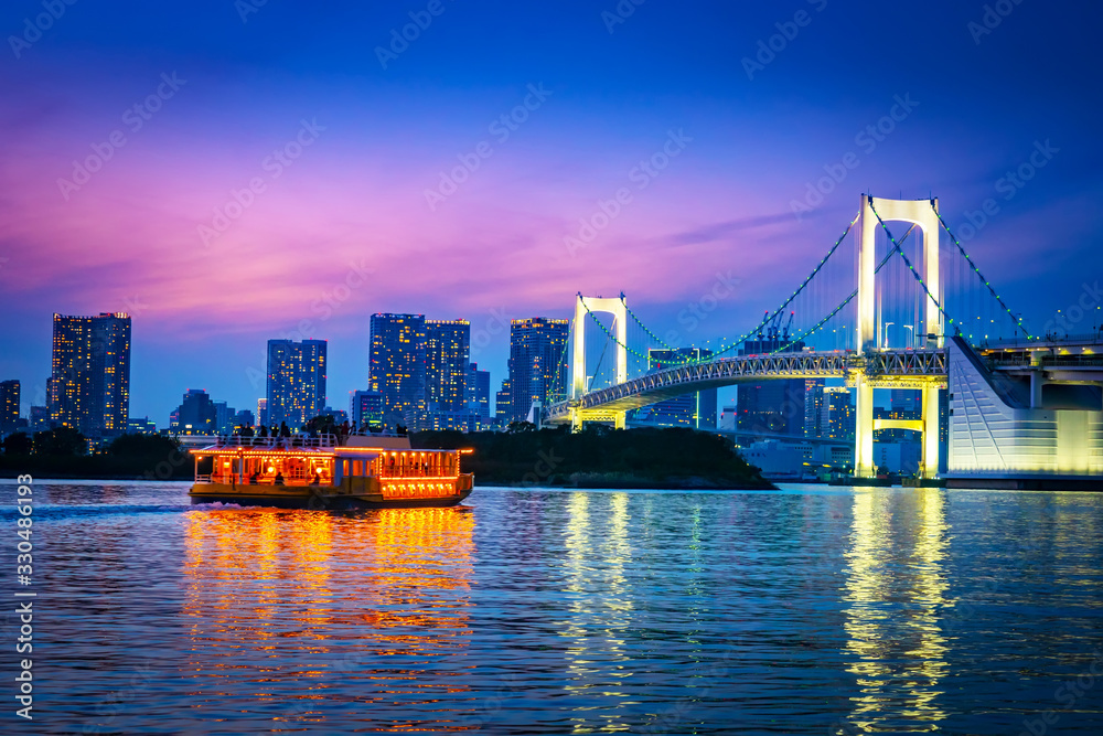Obraz premium Japonia. Tokio. Wyspa Odaiba. Tęczowy most świeci w nocy. Statek pływa po Zatoce Tokijskiej. Wycieczki po Tokio nocą. Tęczowy most na tle nocnego miasta. Wakacje w Japonii.
