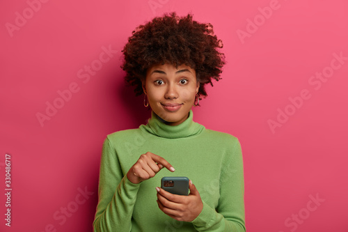 Vászonkép Afro American teenager points at modern smartphone display, recommends download