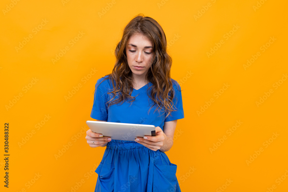 girl in a blue dress with a tablet in her hands on a yellow and orange background with copy space girl in a blue dress with a tablet in her hands on a yellow and orange background with copy space