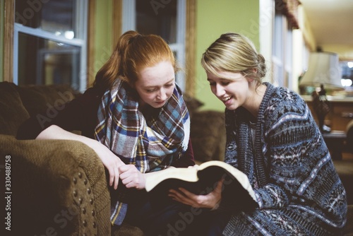 Canvas Print Young female friends sitting on the couch and discussing the Bible